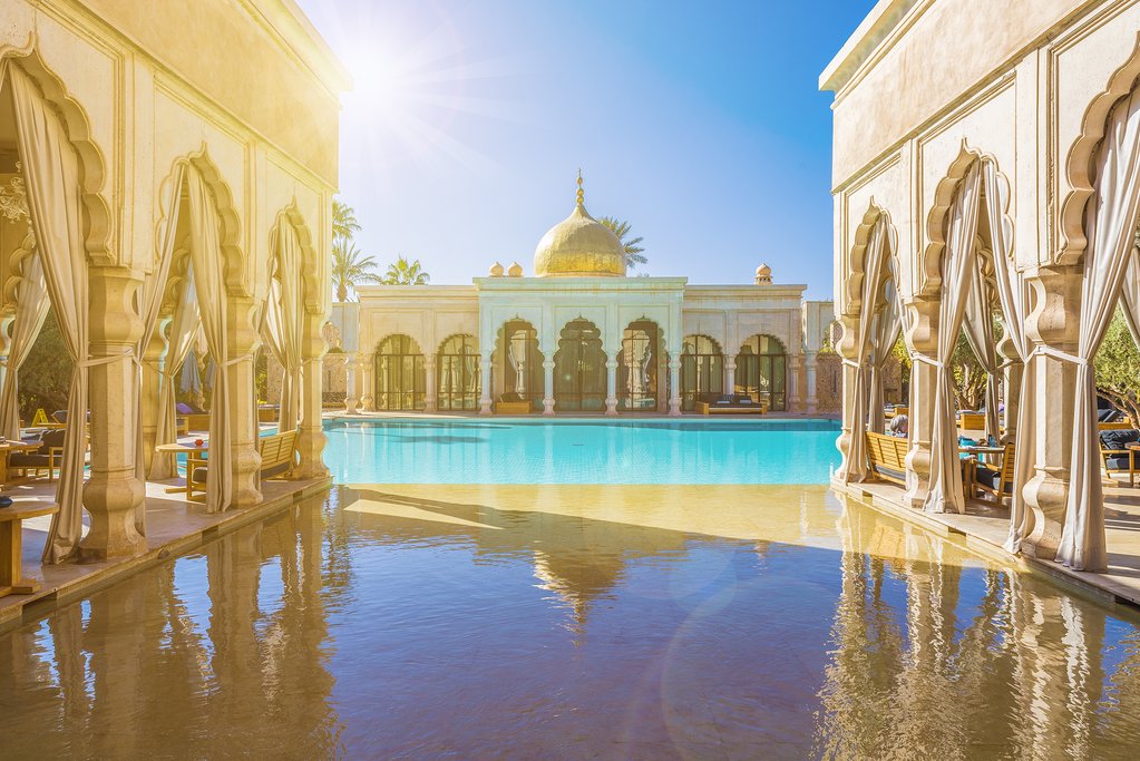 A serene Moroccan palace courtyard with a turquoise reflecting pool, arched colonnades and a gilded dome in Marrakech